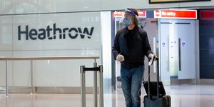 Επιβάτης στο Χίθροου μεταφέρει βαλίτσα φορώντας μάσκα για τον κορωνοϊό