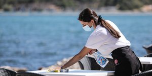 Εργαζόμενη καθαρίζει τραπέζι φορώντας μάσκα