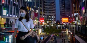 Γυναίκα ανεβαίνει κυλιόμενες σκάλες φορώντας μάσκα για τον κορωνοϊό