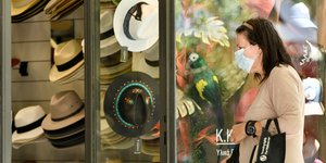 Γυναίκα με μάσκα προστασίας από τη μετάδοση του κορωνοϊού έξω από κατάστημα με καπέλα