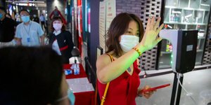 Κινέζα με κόκκινο φόρεμα και κινητό σηκώνει το χέρι της