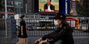 Γυναίκες περπατούν μπροστά από γιγαντοοθόνη που δείχνει τον πρόεδρο της Κίνας