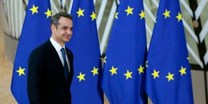Ο Μητσοτάκης περπατά δίπλα από σημαίες της ΕΕ