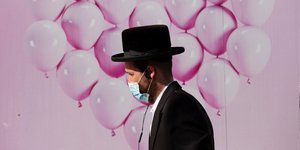 Ραβίνος περπατά δίπλα σε τοιχογραφία με ροζ μπαλόνια, φορώντας μάσκα για τον κορωνοϊό