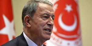 Ο Χουλουσί Ακάρ μπροστά από τουρκικές σημαίες