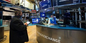 Χρηματιστής στη Νέα Υόρκη κρατά τάμπλετ μπροστά από οθόνες