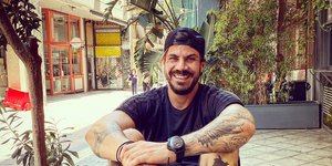 Ο Ακης Πετρετζίκης με καπέλο κάθεται σε παγκάκι