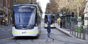 άντρας με μάσκα περπατά ανάμεσα σε τραμ