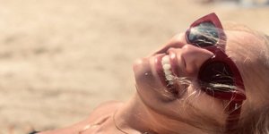 Η ηθοποιός Ντόρα Μακρυγιάννη με γυαλιά ηλίου χαμογελά ξαπλωμένη στην παραλία