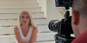 Η Ελένη Μενεγάκη με λευκό outifit μπροστά από μια τηλεοπτική κάμερα