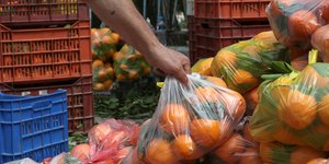 Άνδρας σηκώνει μια τσάντα με πορτοκάλια σε λαϊκή αγορά