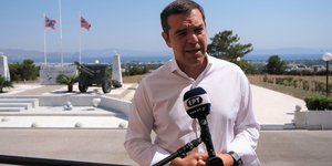 Τσιπρας σε μικροφωνο με λευκο πουκάμισο