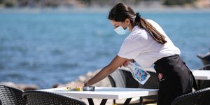 Υπάλληλος καταστήματος απολυμαίνει τραπέζι στη Βουλιαγμένη