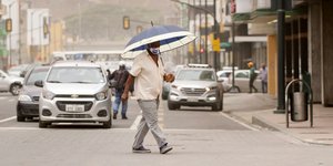 Ανδρας περνά δρόμο στον Ισημερινό κρατώντας ομπρέλα