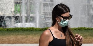 Γυναίκα με μάσκα περπατά μπροστά από συντριβάνι