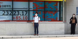 Ιάπωνας στέκεται μπροστά σε οθόνη με αποτελέσματα χρηματιστηρίου
