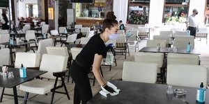 Σερβιτόρα καθαρίζει τραπέζι φορώντας μάσκα για κορωνοϊό