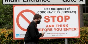 Ανδρας περνά από πινακίδα που προειδοποιεί για τον κορωνοϊό