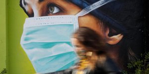 Πολίτης με μάσκα μπροστά από γκράφιτι νοσοκόμας για τον κορωνοϊό στο Μιλάνο