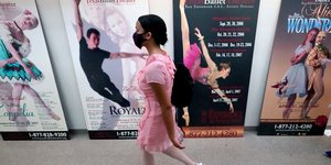Γυναίκα με μάσκα περνά μπροστά από αφίσες για παραστάσεις μπαλέτου
