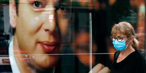 Γυναίκα με μάσκα προστασίας από τον κορωνοϊό στο Βελιγράδι μπροστά σε αφίσα του προέδρου της χώρας Βούτσιτς