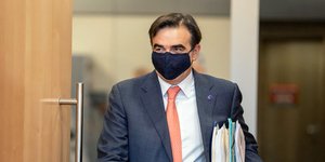 Ο Μαργαρίτης Σχοινάς μπαίνει σε αίθουσα φορώντας μάσκα και κρατώντας έγγραφα