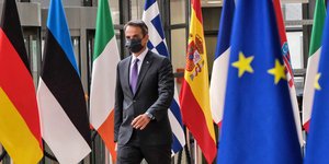 Ο Κυριάκος Μητσοτάκης περπατά ανάμεσα από σημαίες χωρών της ΕΕ φορώντας μάσκα