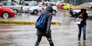 Νεαρό άτομο με τσάντα και κουκούλα στην βροχή