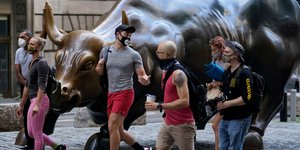 Πεζοί με μάσκες δίπλα από το άγαλμα του ταύρου στην Γουόλ Στριτ