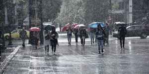 Κόσμος περπατά κρατώντας ομπρέλες