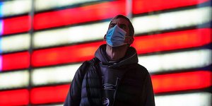 Άνδρας με μάσκα μπροστά από μια φωτεινή σημαία των ΗΠΑ