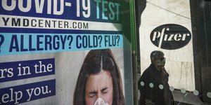 πινακίδα Pfizer και δίπλα μια γυναίκα να περπατά με μάσκα 