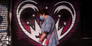 Γυναίκα με μάσκα για τον κορωνοϊό μπροστά από γκράφιτι