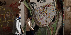 Γυναίκες με μάσκες περπατούν μπροστά από γκράφιτι