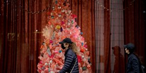Πολίτες με μάσκες στο Λονδίνου περνούν μπροστά από μια στολισμένη βιτρίνα