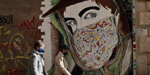 Πολίτες με μάσκα για τον κορωνοϊό μπροστά από γκράφιτι για την πανδημία στην Ιταλία