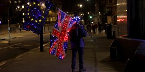 άνδρας κρατά σημαίες Μεγάλης Βρετανίας και ΕΕ με φωτάκια
