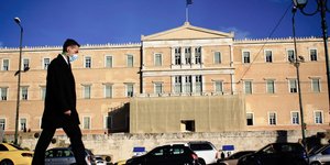 Πεζός περπατά απέναντι από την Βουλή φορώντας μάσκα