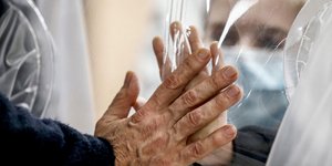 Συγγενής ασθενούς με κορωνοϊό στη Ρώμη, ακουμπά το χέρι του πίσω από πλαστικό παραπέτασμα