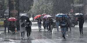 Πολίτες περπατούν με ομπρέλες κάτω από βροχή