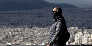 Ανδρας με μάσκα περπατά με φόντο την Αθήνα