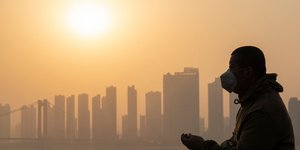 Ανδρας με μάσκα στις όχθες ποταμού της Ουχάν της Κίνας με την ανατολή του ήλιου