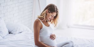 Έγκυος γυναίκα στο κρεβάτι του σπιτιού της κρατάει την φουσκωμένη κοιλιά της