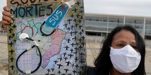 Γυναίκα με μάσκα κρατά πλακάτ για τους νεκρούς από κορωνοϊό στην Βραζιλία 