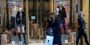 Γυναίκα περνά μπροστά από βιτρίνα κρατώντας τσάντες