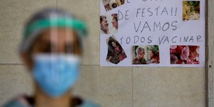 γυναίκα με μάσκα στη Βραζιλία μπροστά σε χαρτόνι που γράφει για τον εμβολιασμό