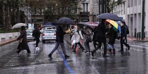 Κόσμος περπατά στον δρόμο με ομπρέλες