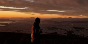 Άνδρας μπροστά στη θέα του λεκανοπεδίου της Αθήνας το ηλιοβασίλεμα