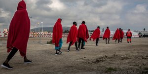 Μετανάστες περπατούν έχοντας κόκκινες κουβέρτες πάνω τους