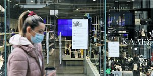 Γυναίκα περνά μπροστά από βιτρίνα κρατώντας καφέ